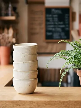 A stack of ceramic cups next to a potted fern on the counter